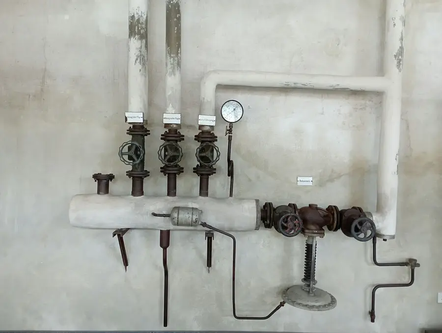 Pipes with shut-off valves and a pressure gauge on a bare concrete basement wall