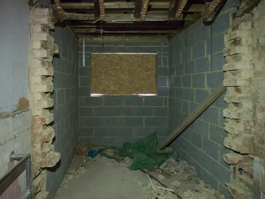 Unfinished basement with concrete block walls and a boarded-up window