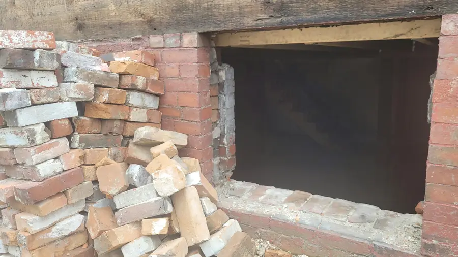 Brick and rubble foundation wall with loose bricks stacked in front of an opening