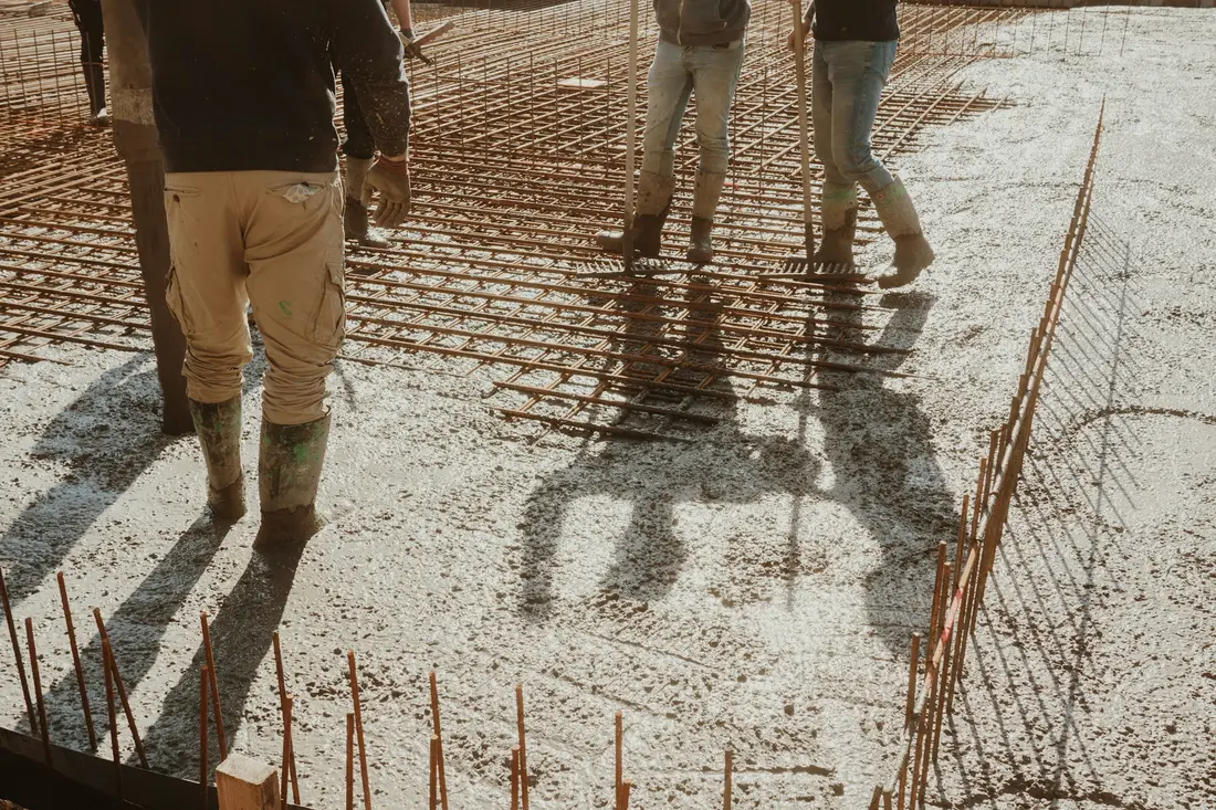 Workers in rubber boots walking across a freshly poured concrete floor