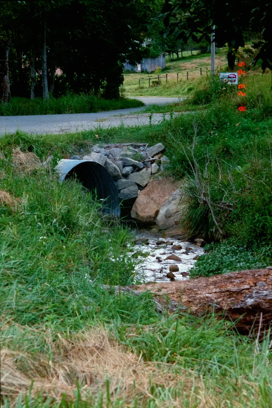 Water flowing out of a concrete culvert into a stream among rocks and grass