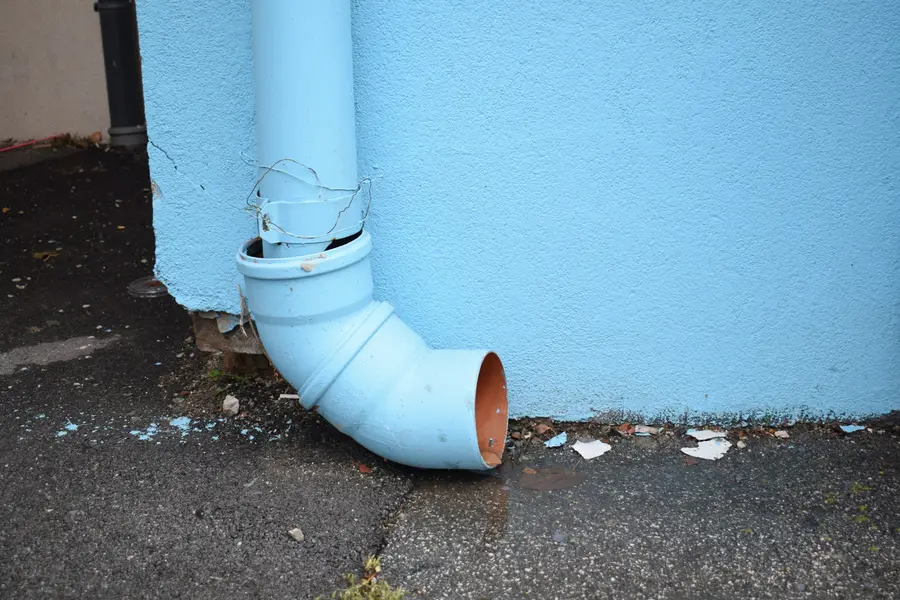 Downspout elbow ending right at the base of a pale blue wall