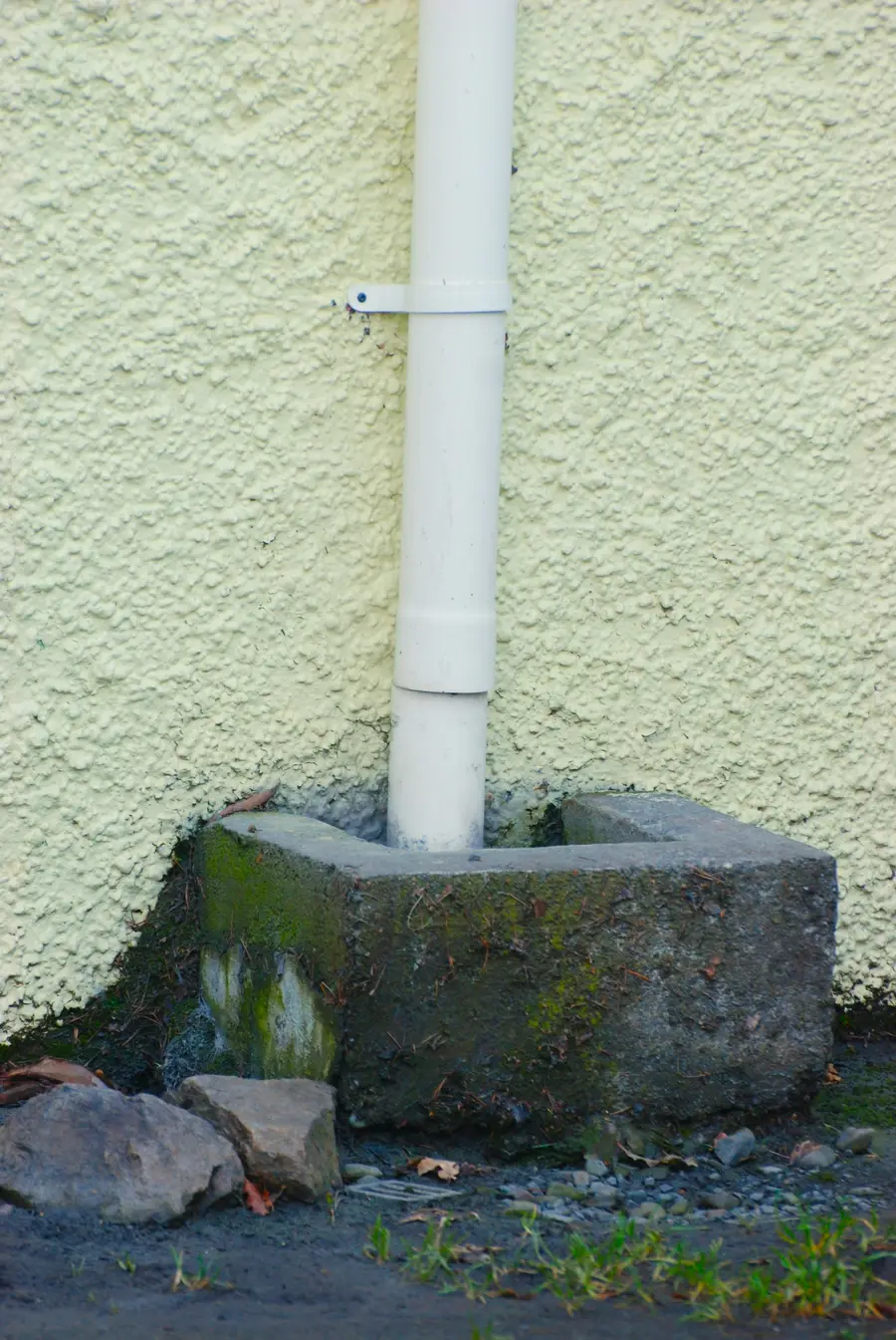 Downspout running into a concrete block at the base of a wall