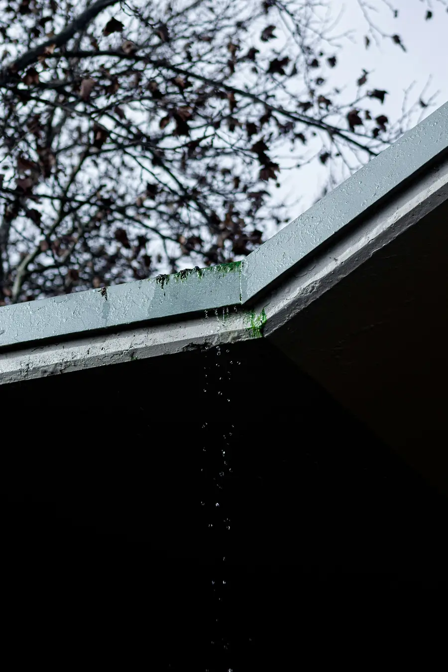 Water dripping from the edge of a dark roof overhang