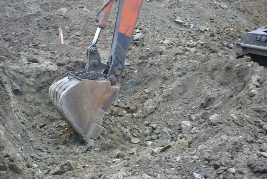 Excavator bucket digging into stony soil at the bottom of an excavation