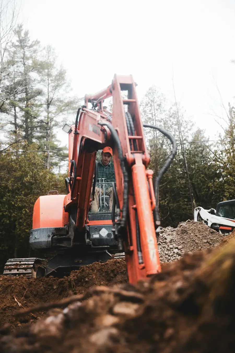 Red compact excavator at the edge of a trench with an operator in the cab