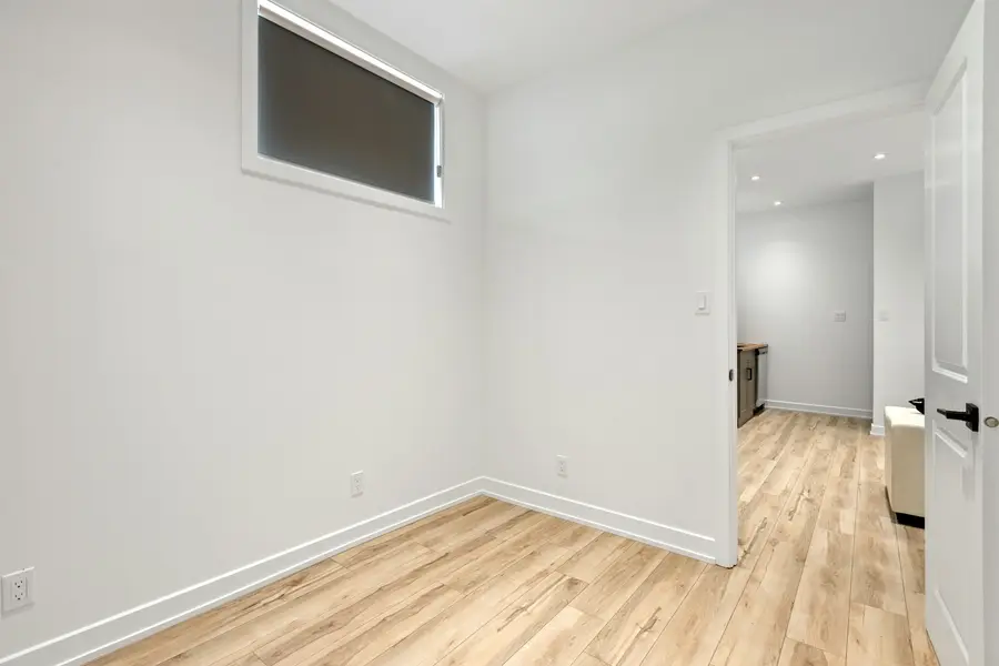 Finished basement room with white walls, a high window and a light wood-look floor