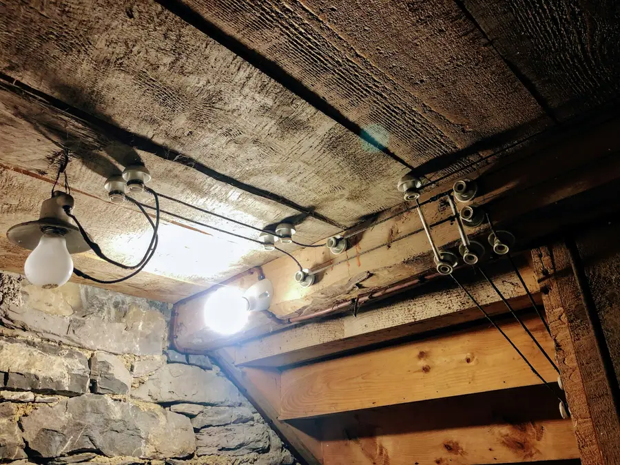 Old basement ceiling with wooden joists, exposed wiring and a bare bulb