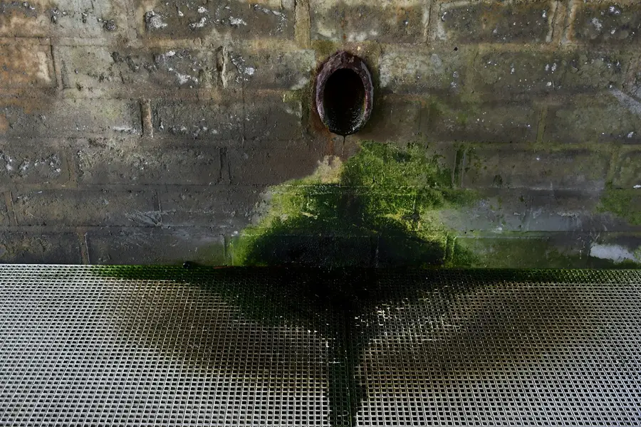 Drain pipe sticking out of a stone wall above a dark stain of running water