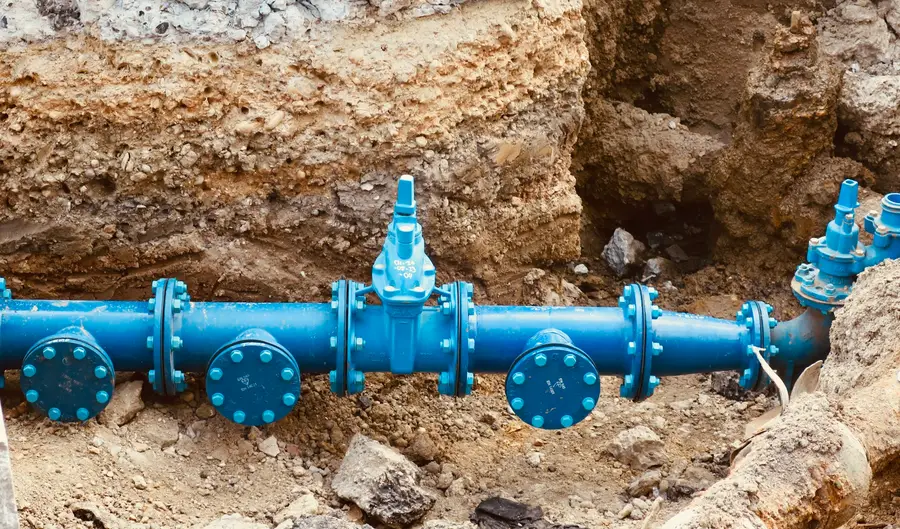 Blue water line with valves exposed at the bottom of an excavated trench
