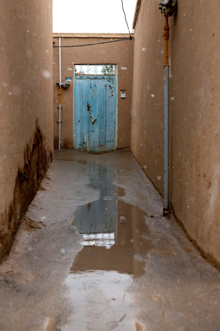 Narrow concrete corridor with water pooled on the floor and stained walls