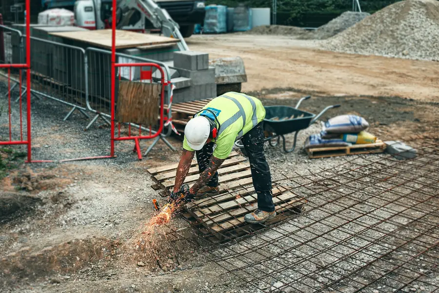 Worker in a high-visibility vest and hard hat kneeling to cut reinforcing mesh