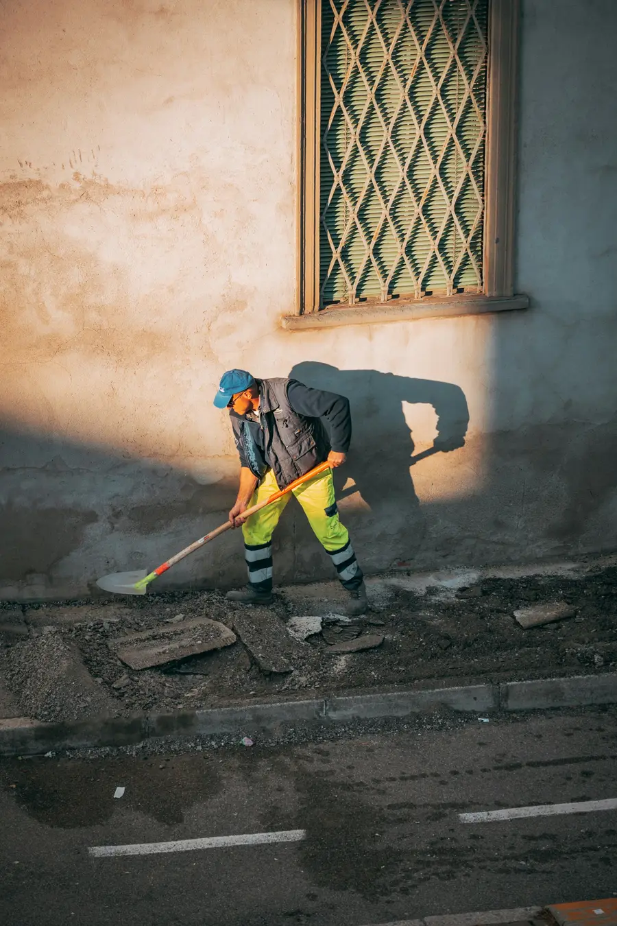 Worker in high-visibility trousers shovelling gravel against a parged wall